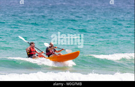 Cornwall, England, UK. UK Weather: Thursday 27th June 2019. Hot sunshine arrives along with heatwave temperatures with car thermometers showing 31C along the Cornish coastline. Beach goers enjoying  sea kayaking on the waves during hot sunshine and heatwave temperatures at Harlyn Bay Beach near Padstow, Cornwall Stock Photo