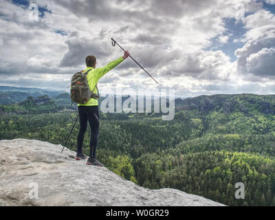Slim body trek runner with backpack and trekking poles walk mountain trail. Rocky part of path with view into distance. Stock Photo