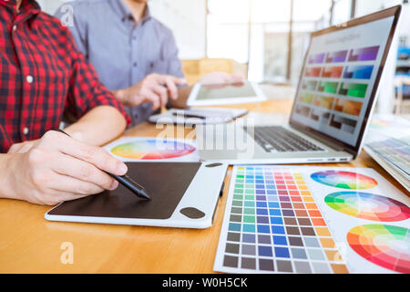 Teamwork of young creative designers working on project together and choose color swatch samples for selection coloring on digital graphic tablet at w Stock Photo