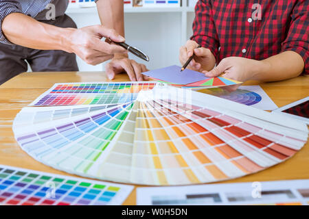 Teamwork of young creative designers working on project together and choose color swatch samples for selection coloring on digital graphic tablet at w Stock Photo