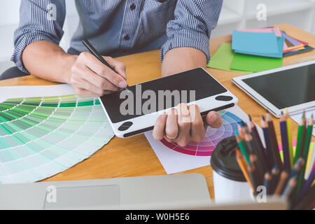 Young creative graphic designer working on project architectural drawing and color swatches, selection coloring on graphic chart with work tools and e Stock Photo