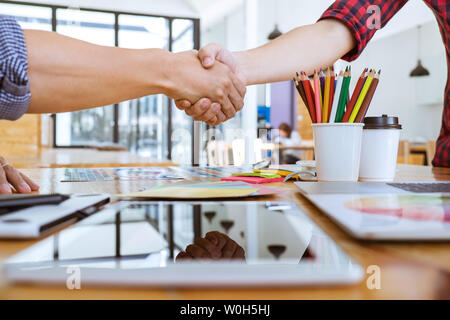 Cooperation of Young creative graphic designer working on workspace and shaking hands after successful of new project, putting hands together. Stock Photo