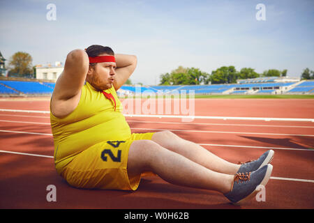 The fat man in sportswear doing abdominal exercises in the stadium in the summer. Winner motivation concept. Stock Photo