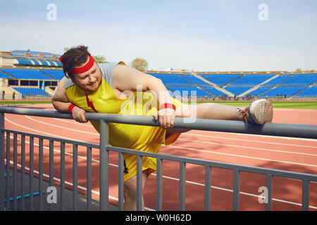 Fat funny man in sportswear doing stretching at the stadium. Stock Photo