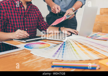Teamwork of young creative designers working on project together and choose color swatch samples for selection coloring on digital graphic tablet at w Stock Photo
