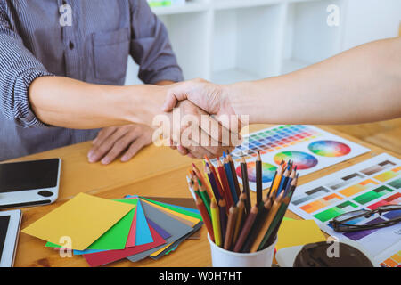 Cooperation of Young creative graphic designer working on workspace and shaking hands after successful of new project, putting hands together. Stock Photo