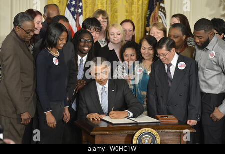 US President Barack Obama, surrounded by workers, signs an Executive Order requiring federal contracts to pay a minimum wage of $10.10 during a ceremony in the East Room of the White House, February 12, 2014, in Washington, DC. Obama called on Congress to extend the wage to all by passing the Harkin-Miller Bill.      UPI/Mike Theiler Stock Photo