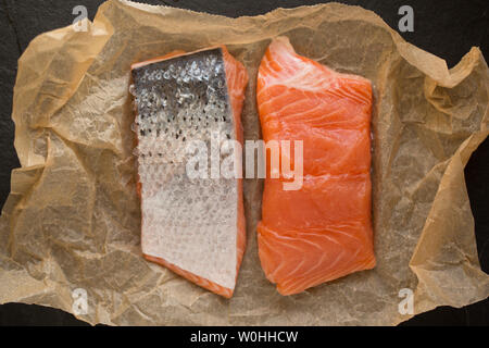 Two fillets of raw farmed Scottish salmon bought from a supermarket in the UK showing the skin side and the flesh side. Displayed on brown baking pape Stock Photo