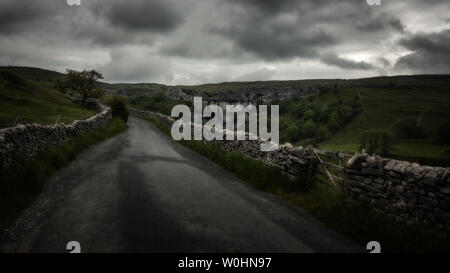 Atmospheric, dramatic shot up the steep road to the side of Malham Cove on a damp June day with limestone drystone wall, Yorkshire Dales, UK