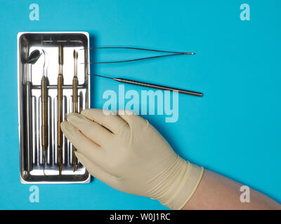 Dental instruments in tray and dentist hand on blue background Stock Photo