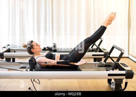 Adult woman wearing black outfit doing the hundred pilates exercise on reformer bed in workout room Stock Photo