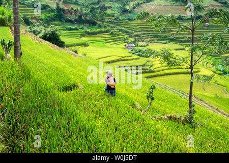 Mu Cang Chai, Vietnam - Sep 07 2017 : Grandmother carrying grandson walking in green rice field terraced on tribe valley Stock Photo