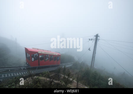 Sapa, Vietmam - Sep 08 2017 :  Red tram retro style run to the top hill with passenger on foggy day at Fansipan Legend Stock Photo
