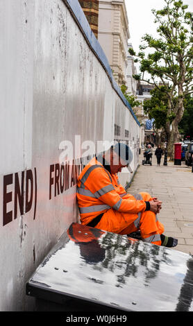 Workman taking a break outside construction site hoarding, London, England, UK Stock Photo