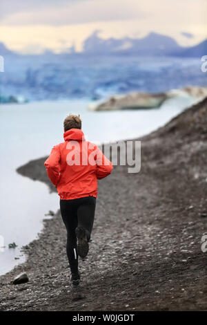 Runner man trail running training for run in beautiful nature landscape. Fit male athlete jogging and cross country running by icebergs in Jokulsarlon glacial lake in Iceland. Stock Photo