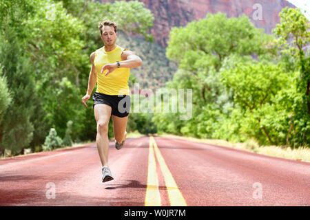 Running man sprinting looking at heart rate monitor smartwatch on run. Man jogging outside looking at his sports smart watch during workout training for marathon. Fit male fitness model in his 20s. Stock Photo