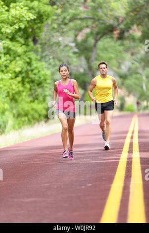 People running on road. Sport and fitness runners woman and man training for marathon run doing high intensity interval training sprint workout outdoors. Athletes sports models fit and healthy. Stock Photo