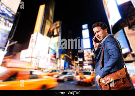 Young urban professional business man talking on smart phone onTimes Square, Manhattan, New York City. Young hip male businessman in casual suit in at night outdoors. Stock Photo