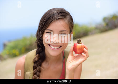 Girl showing natural fresh cashew nut apple fruit. Asian Chinese woman portrait smiling holding a freshly picked apple fruit from the tropical tree where the cashew nut come from. Caribbean food. Stock Photo