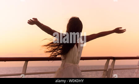 Cruise ship vacation woman enjoying sunset on travel at sea. Free happy woman looking at ocean in happy freedom pose with arms out. Woman in dress on luxury cruise liner boat.