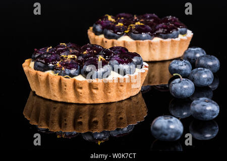 Two blueberry and custard tarts with fresh blueberries on black granite with reflections Stock Photo