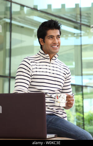 Indian man using a laptop and having a cup of coffee Stock Photo