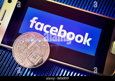 Facebook logo on a smartphone screen and coin, libra cryptocurrency Stock Photo