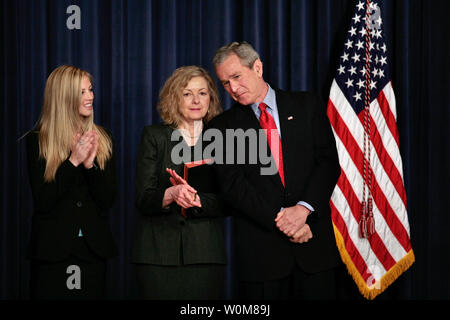 President George W. Bush leans over to chat with Vicki Lazear, wife of Eddie Lazear, who was just sworn in as Chairman of the Council of Economic Advisors at the EEOB in Washington on March 6, 2006.  Lazear's daughter Julie is at left.   (UPI Photo/Ken Cedeno) Stock Photo