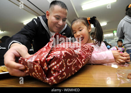 Information Systems Technician 1st Class Oscar Bernuy, assigned to the U.S. 7th Fleet staff embarked aboard the amphibious commad ship USS Blue Ridge (LCC 19), helps a child open a gift at the Shunko Gakuen Boys and Girls Home in Yokosuka, Japan, December 22, 2010, during a community service project. Blue Ridge is the flagship for Commander, U.S. 7th Fleet. UPI/Brian A. Stone/US Navy. Stock Photo