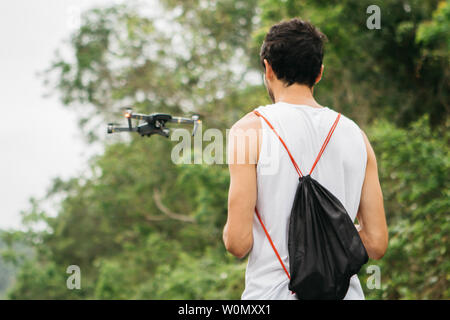 Back view of a young man operating a drone by remote control in the park. Stock Photo