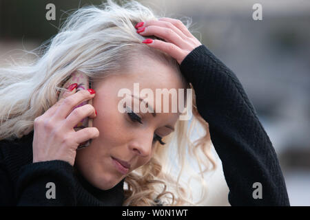 Stressed upset young woman talking on a mobile running her hand through her long curly blond hair with a worried expression