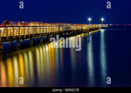 Night time long exposure image of people walking on a jetty with beautiful light reflections in the water. Andernos les Bains, Arcachon Bay, France Stock Photo