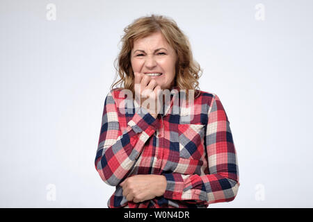 Anxious mature woman biting nails, beingdesperate or frightened. Mother is worried about her children exam results. Studio shot Stock Photo