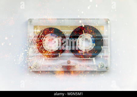 Concept image of a transparent plastic compact cassette audio tape fizzing with sparks and fire as if energised, on a white background Stock Photo