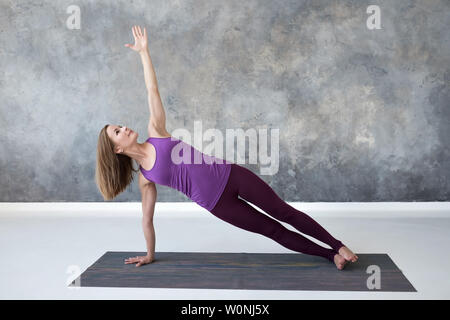 Slim caucasian woman doing side plank yoga pose in fitness studio Stock Photo