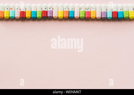 Row of capsule on a pastel paper pink background. Copyspace. Border of Funny colored medecines Stock Photo