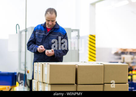 Factory worker taking notes while checking boxes in factory warehouse Stock Photo