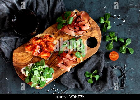 Bruschetta set for wine. Variety of small sandwiches served with red wine on rustic wooden board over dark background. Top view with copy space. Stock Photo
