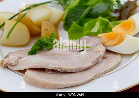 Roast pork slices with baby new potatoes a leafy salad and hard-boiled eggs Stock Photo
