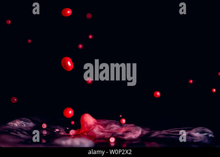 Splash of red colored milk droplets that look almost like jellybeans in close up macro high resolution isolated against a black background Stock Photo