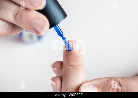 A mother paints her young girl's hands with blue and pink nailpolish, viewed against an isolated white background Stock Photo
