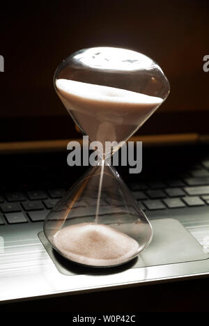 An hourglass sits on a laptop computer. Stock Photo