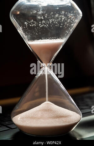 An hourglass sits on a laptop computer. Stock Photo