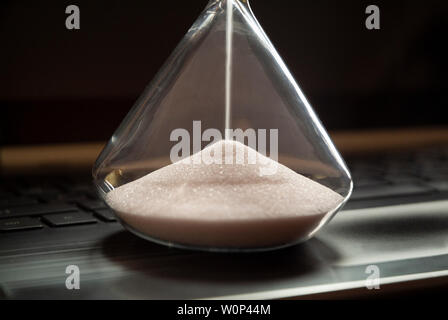 An hourglass sits on a laptop computer. Stock Photo