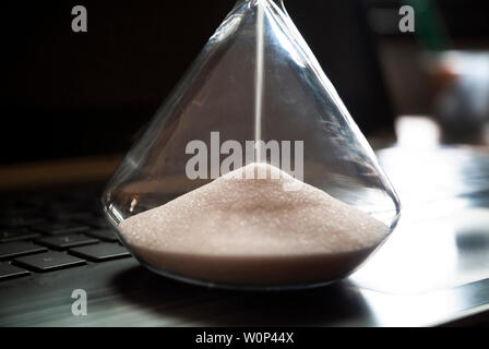 An hourglass sits on a laptop computer. Stock Photo