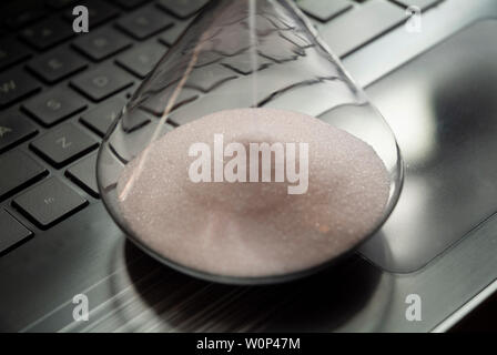 An hourglass sits on a laptop computer. Stock Photo