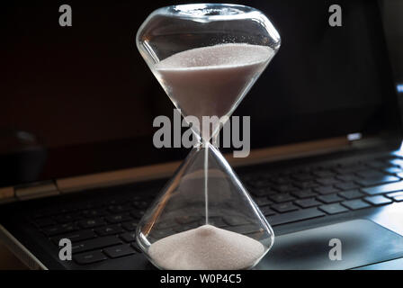 An hourglass sits on a laptop computer. Stock Photo
