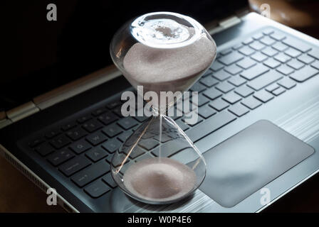 An hourglass sits on a laptop computer. Stock Photo