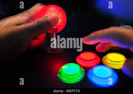 A red lighted arcade joystick and four button layout push buttons being played by a video gamer on a retro arcade machine. Stock Photo