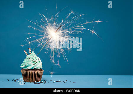 Birthday Cupcake with sparkler against a blue background. Stock Photo
